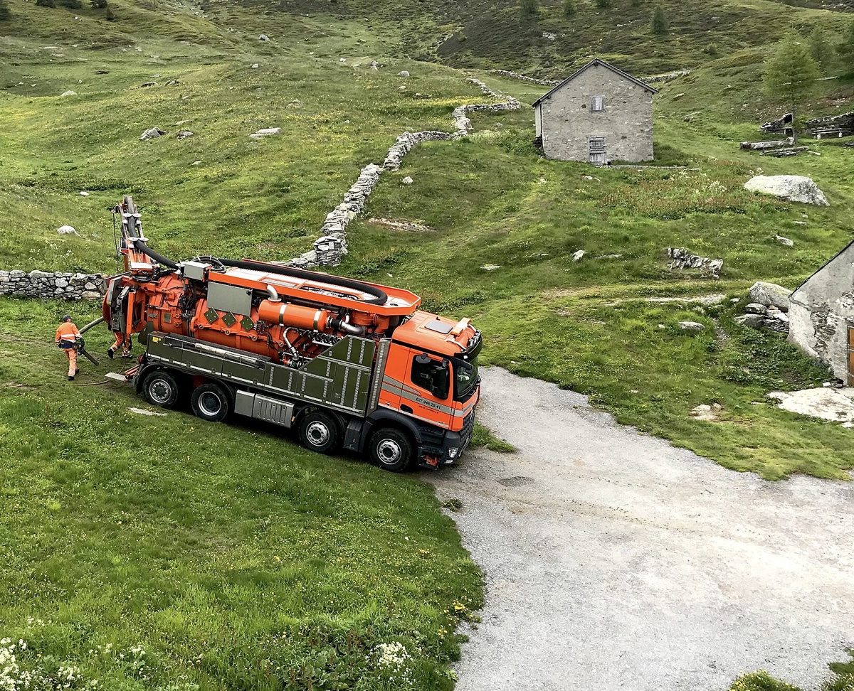 Camion de vidange en intervention sur un terrain en pente, près de maisons de montagne