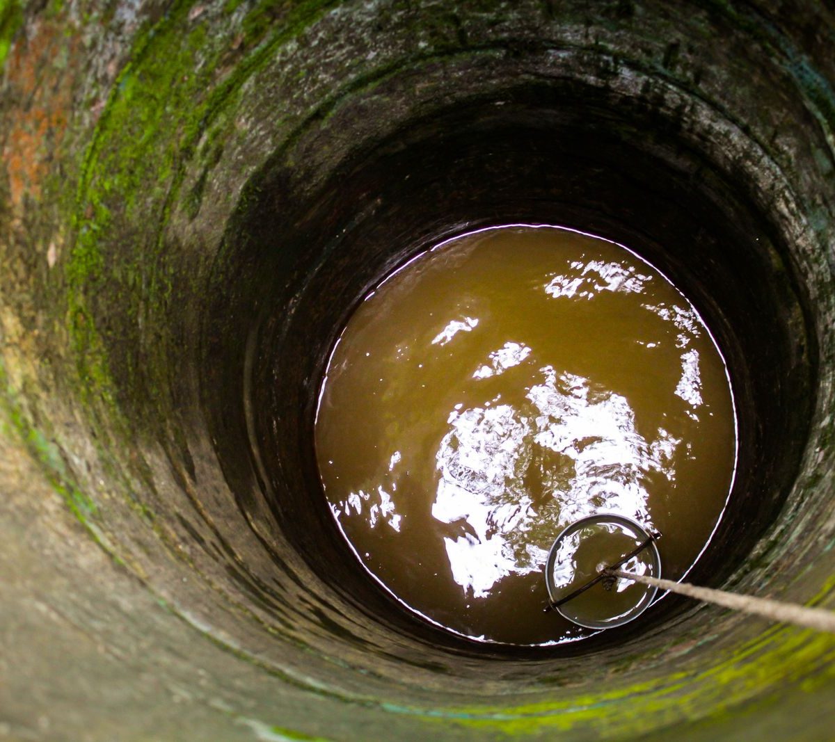 Puits domestique en pierre, eau visible au fond avec seau sur corde