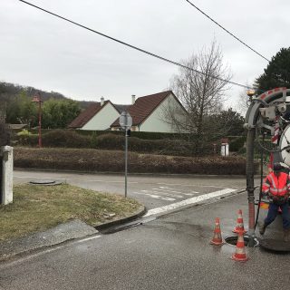 Camion hydrocureur et agent en intervention sur un regard, devant une maison individuelle