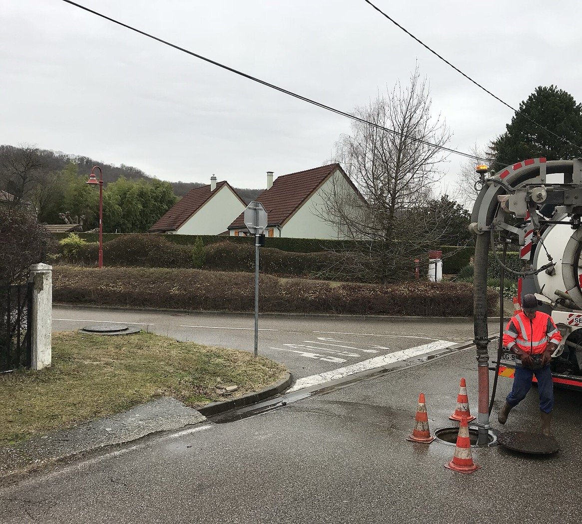 Camion hydrocureur et agent en intervention sur un regard, devant une maison individuelle