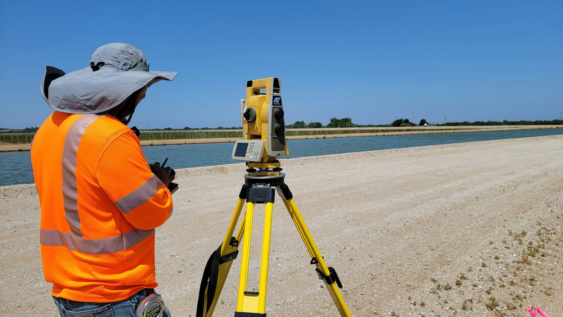 géomètre en tenue de chantier qui règle une station totale sur trépied pour un relevé de terrain en extérieur